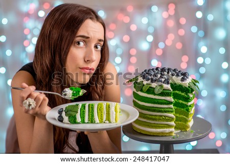 Sad girl thinking eat or not to eat happy birthday cake sitting on festive light background