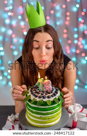 Eighteen girl with happy birthday cake blowing up candles on festive light background