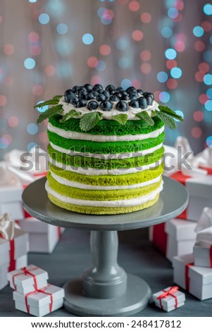 Nice sponge happy birthday cake with mascarpone and grapes with on the cake stand with gift boxes on festive light bokeh background