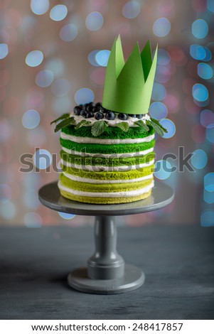 Nice sponge happy birthday cake with mascarpone and grapes on the cake stand with crown on festive light bokeh background