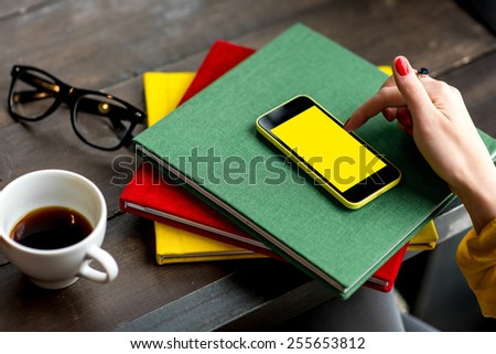 Woman using smart phone on the table with colorful books. Phone with empty screen for your application