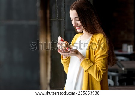 Young smiling woman dressed in yellow sweater eating ice cream in the dark cafe interior