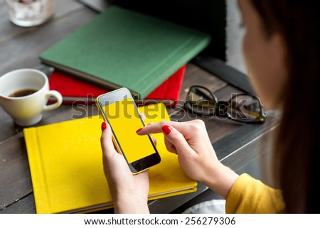 Woman using smart phone on the table with colorful books. Phone with empty screen for your application