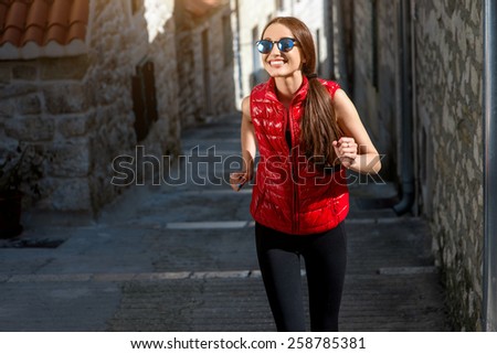 Young sporty woman running in the old city street in the morning