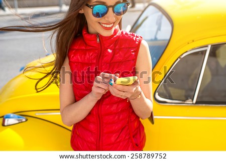 Woman using smart phone near her yellow old fashioned car on the street