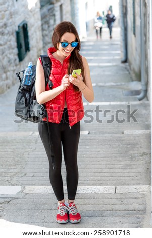 Young woman in red sportswear looking where to go with smart phone traveling in the old city center. Traveling application concept