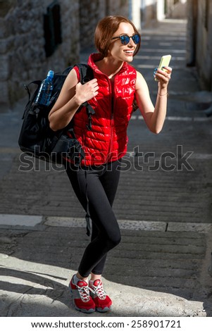 Young woman in red sportswear looking where to go with smart phone traveling in the old city center. Traveling application concept