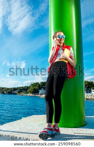 Sport woman in red vest using mobile phone while standing near the green lighthouse on the beach