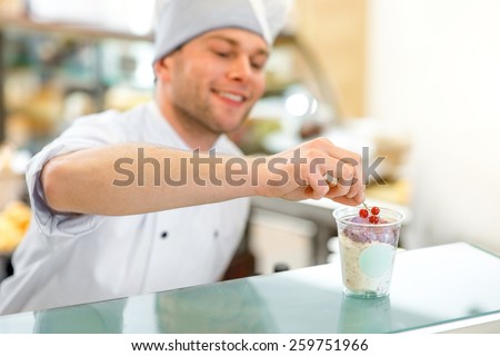 Handsome confectioner decorating ice cream with berry in the store
