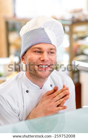 Handsome confectioner in uniform smiling in the pastry shop