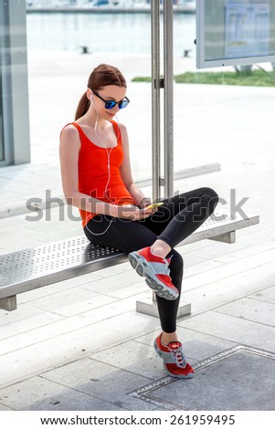 Young sport woman with phone waiting at the bus station