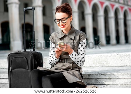 Young woman dressed in coat and glasses with travel bag using phone on the stairs at Republic square in Split city