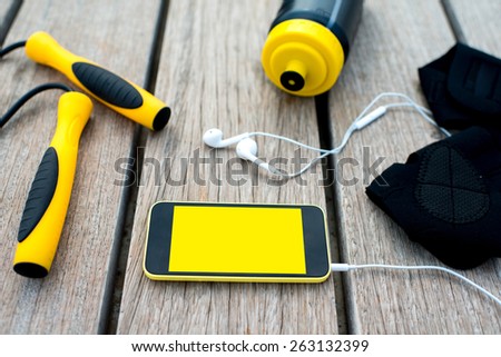 Mobile phone with empty screen on the wooden desk surrounded with sport equipment. Sport mobile application concept
