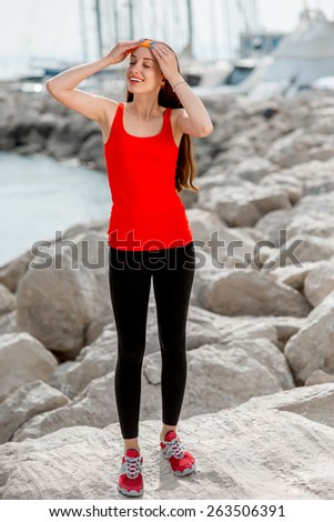 Young sport woman in red shirt standing on the rocky beach in the morning