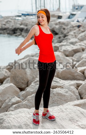 Young sport woman in red shirt warming up on the rocky beach in the morning