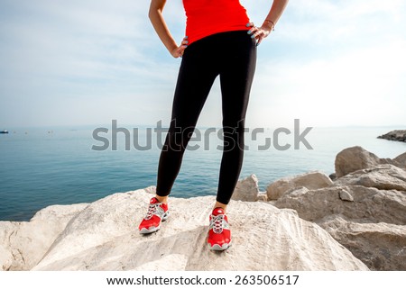 Sporty woman legs in red sneakers on the rocky beach. Back view