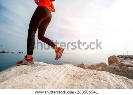 Sport woman running on the rocky beach. Legs close up plan