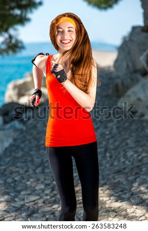 Young smiling sport woman in red shirt running on the rocky path near the sea
