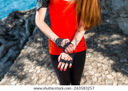 Woman putting on sports gloves in the park near the sea. Close up plan without face