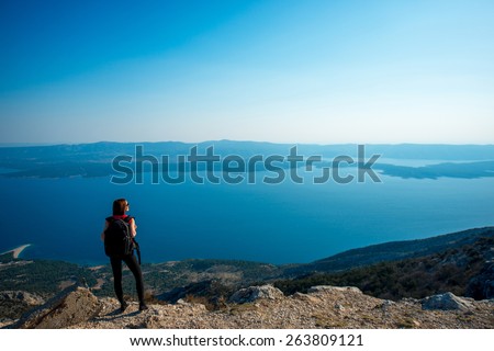 Young woman traveler with backpack standing on the top of mountain. General back view