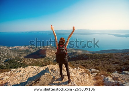 Young sport woman traveler raising hands on the top of island mountain. General back view