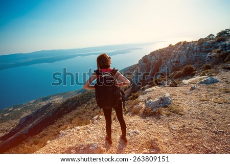 Young woman traveler with backpack standing on the top of mountain on the sunset