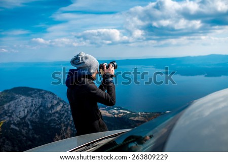 Man photographing lanscapes standing near his car on the top of mountain