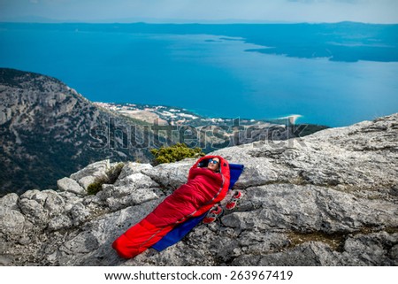 Young woman lying in red sleeping bag on the rocky mountain