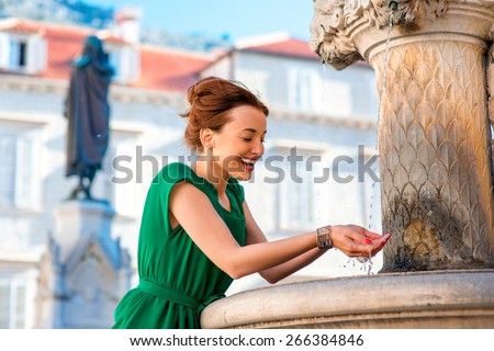 Young woman in green dress drinking water from classical fountain in the Dubrovnik city in Croatia