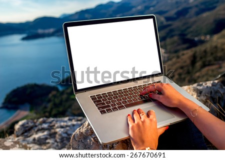 Woman working with laptop on the top of mountain with beautiful landscape on background. Blogging concept