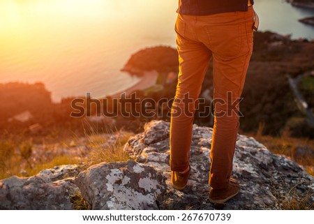 Men\'s legs in the brown shoes standing on the mountain on the sea scape background on the sunset