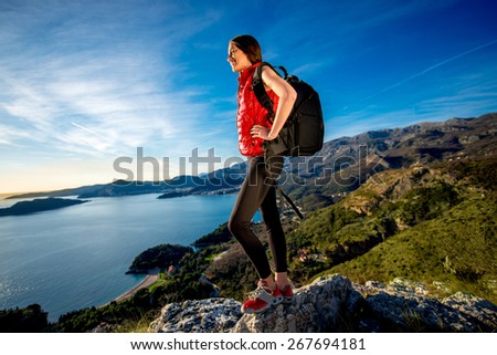 Sports woman in red vest with backpack standing on the top of mountain on the sunset.