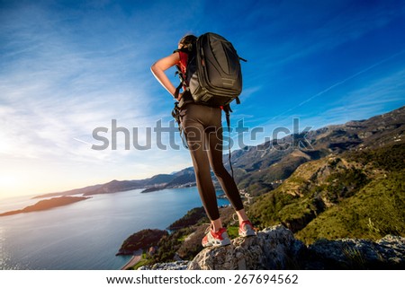 Sports woman in red vest with backpack standing on the top of mountain on the sunset.