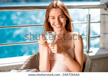 Young and smiling woman drinking milk on the balcony on blue water background
