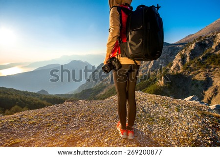 Young traveler photographer with photo camera and backpack standing on the top of mountain. Focused on the photo camera