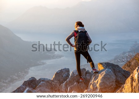 Young traveler with backpack standing on the big stones on the mountain and observing locality