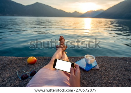 Woman holding phone lying on the pier at beautiful sunset