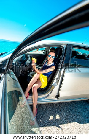 Young smiling woman in colorful clothes and sunglasses making self portrait sitting in the car near the sea