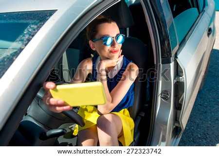 Young smiling woman in colorful clothes and sunglasses making self portrait sitting in the car.
