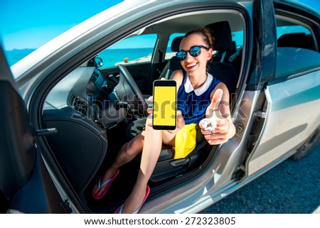 Young and cute woman showing phone screen sitting in the car. Navigation or travel phone program concept.
