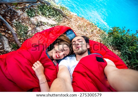 Young couple lying in red sleeping bags near the sea