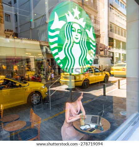 ATHENS, GREECE, MAY 04, 2015: Woman sitting in the Starbucks cafe with big Starbucks logo and yellow cabs reflection on the window .