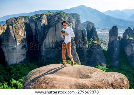 Professional well-dressed photographer on the top of mountain on beautiful scenic clif background near Meteora monasteries in Greece.
