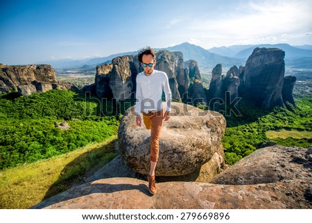 Well-dressed man walking on the rocky mountain on beautiful scenic clif background near Meteora monasteries in Greece.