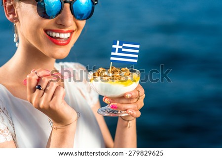 Smiling woman eating traditional greek yogurt with nuts and honey outdoors on blue sea background
