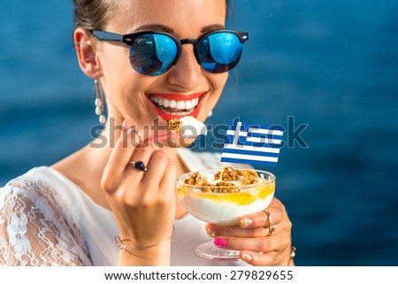 Smiling woman eating traditional greek yogurt with nuts and honey outdoors on blue sea background