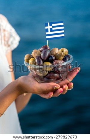 Holding plate with green and black local greek olives on blue sea background