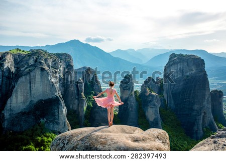 Young woman in pink dress enjoying nature on the mountains near Meteora monasteries in Greece, soft focus