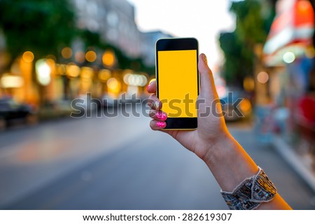 Woman hands using mobile smart phone with empty screen on street evening light with colorful bokeh background
