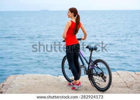 Sport woman in red shirt standing with bicycles on the concrete seacoast